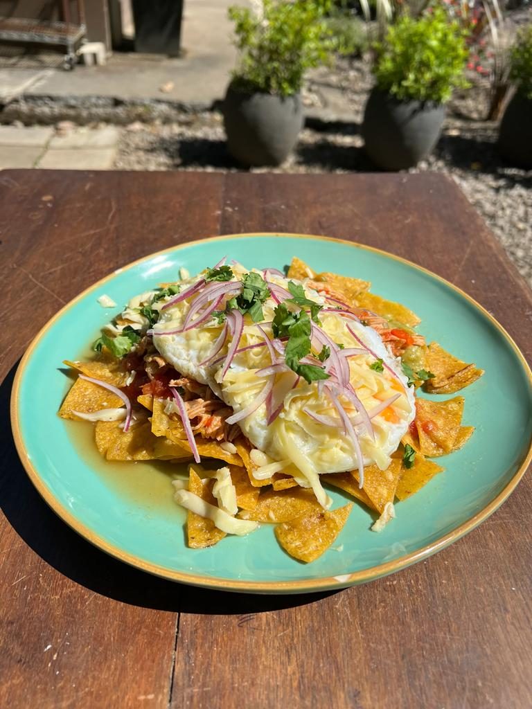 Chilaquiles con pollo y huevo sobre un plato turquesa en una mesa del jardín